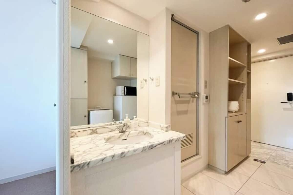 Une salle de bain moderne avec un lavabo en marbre, un grand miroir, une douche à l’italienne et un meuble encastré.