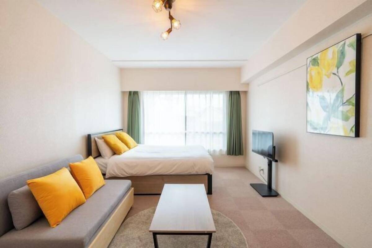 Une chambre d’hôtel avec un lit, un canapé, une table basse, une télévision et une fenêtre avec des rideaux.