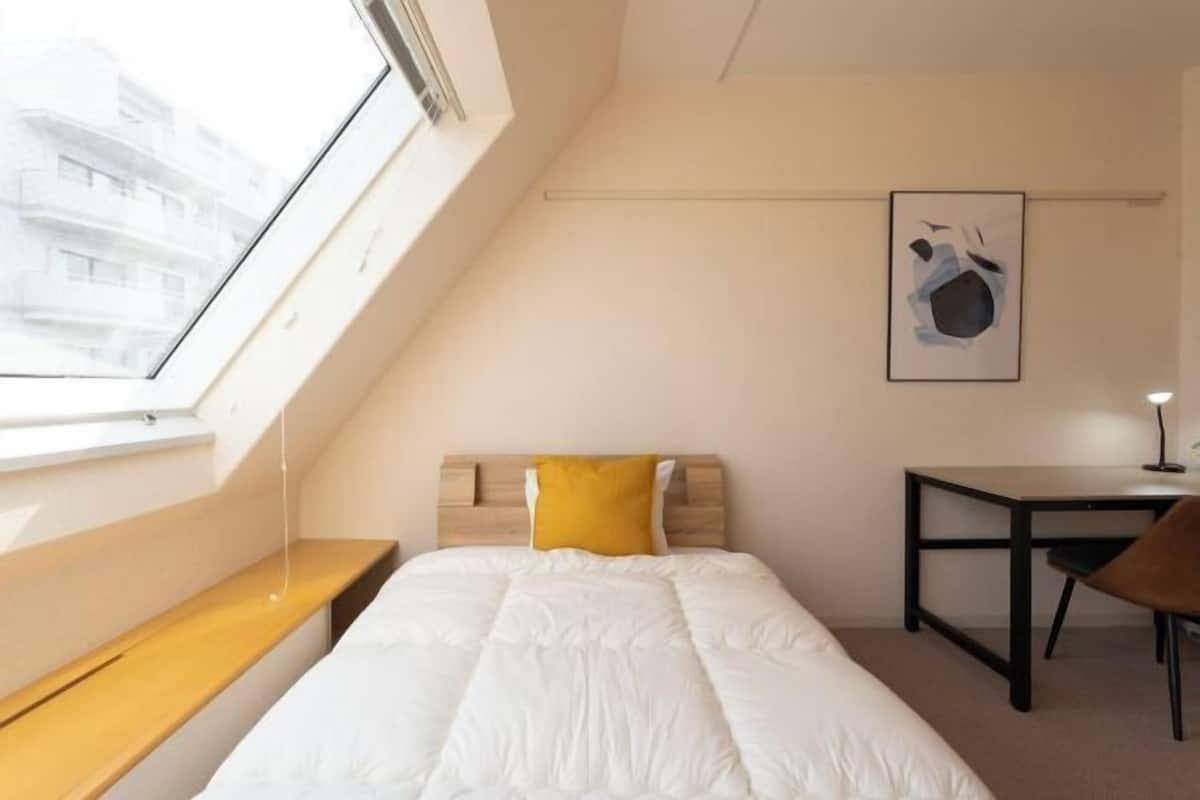 Une pièce comprenant un lit, un bureau, une chaise, une fenêtre et un tableau accroché au mur.