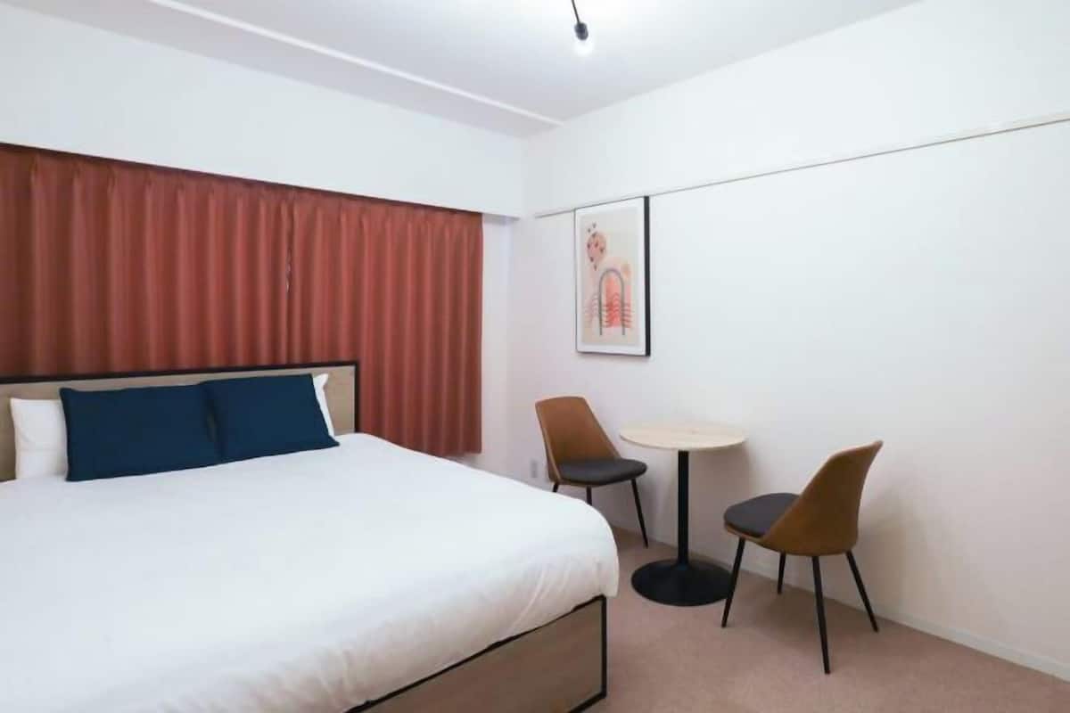 Une chambre d’hôtel avec un lit, deux chaises, une petite table et un tableau encadré au mur.