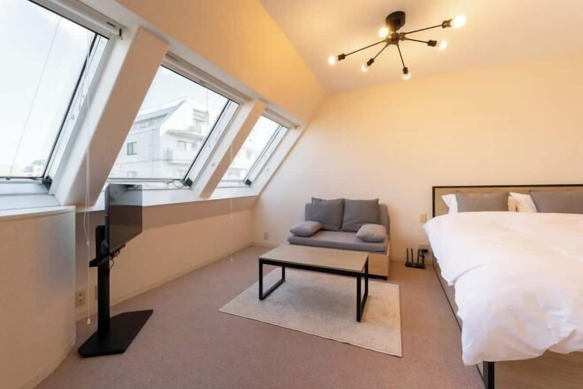 Ein modernes Schlafzimmer mit Bett, Sofa, Schreibtisch und Deckenleuchte.