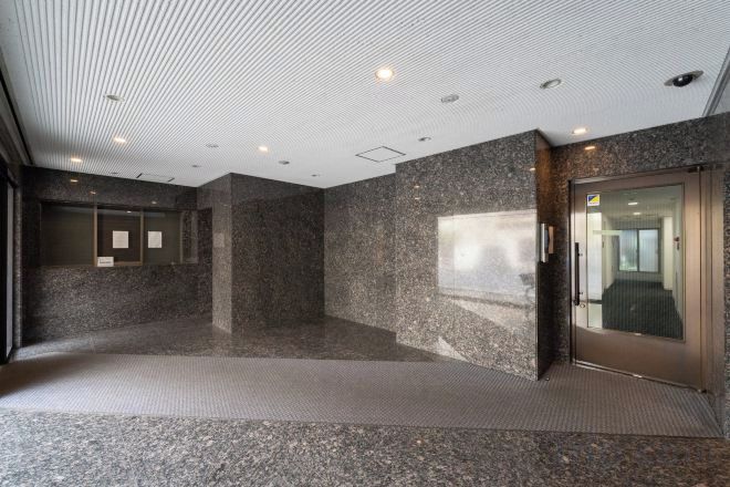 Een ruime lobby met een granieten vloer, een glazen lift en een informatiepaneel aan de muur.
