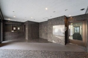 A spacious lobby with a granite floor, a glass elevator, and a wall-mounted information board. - Fujiterrace Yoga (Tokyo)