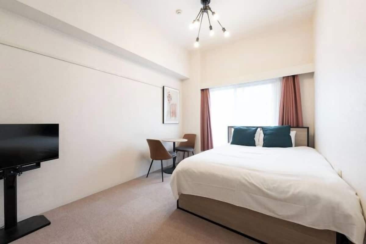 Une chambre d’hôtel équipée d’un lit, d’un bureau, d’une chaise, d’une télévision et d’une fenêtre avec des rideaux.