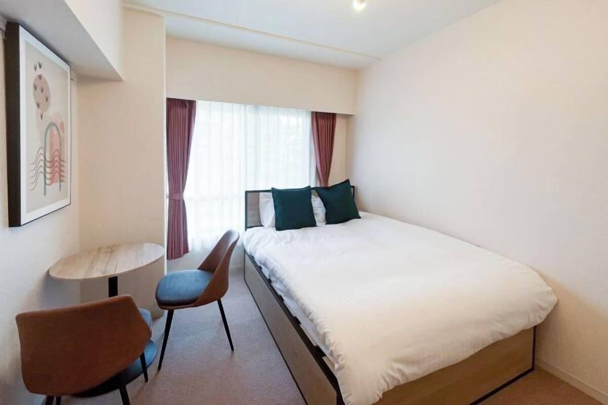 Une chambre d’hôtel avec un lit, une chaise, une petite table et une fenêtre avec des rideaux.