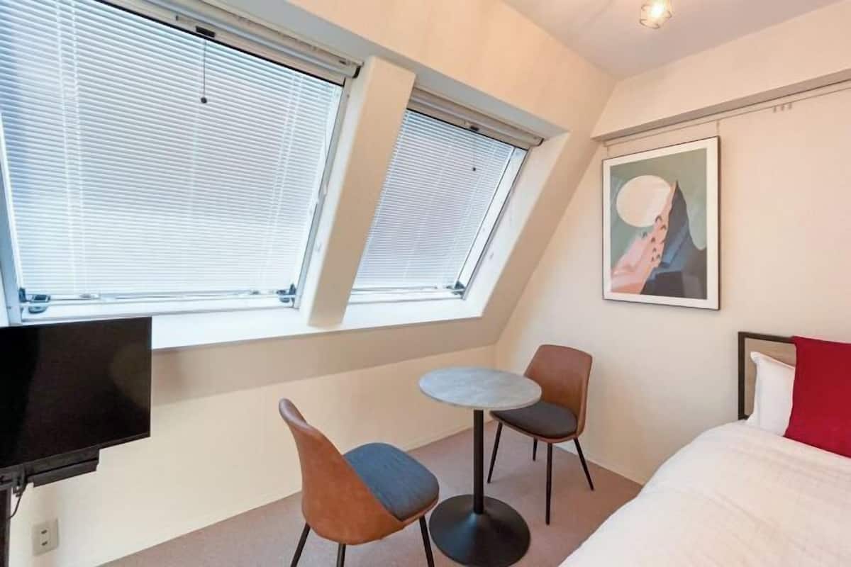 Ein Hotelzimmer mit einem Bett, einem Fernseher, zwei Sesseln, einem kleinen Tisch und einem Bild an der Wand.
