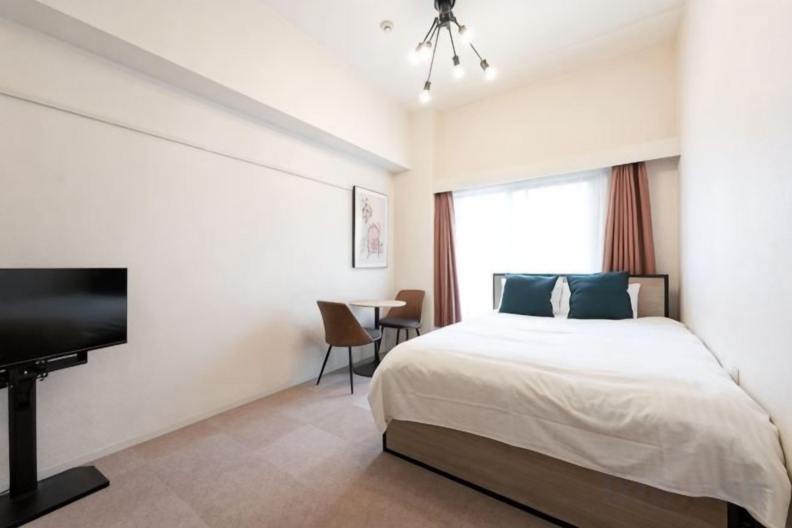 Habitación de hotel con cama, escritorio, silla, televisión y ventana con cortinas.