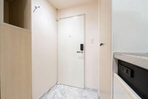 A narrow hallway with a door, a wooden panel wall, and a white appliance on the right. - Fujiterrace Yoga (Tokyo)
