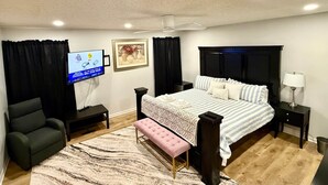 Un dormitorio con cama, televisor, escritorio, silla y ventana con cortinas.