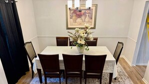 Un comedor con una mesa dispuesta para cuatro, rodeada de sillas de madera oscura, un tapete estampado y un jarrón de flores.