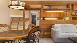 A cozy room with a wooden dining table, chairs, a sofa, and a hanging light fixture. - Outpost: Larkspur 1212 (Wilson)