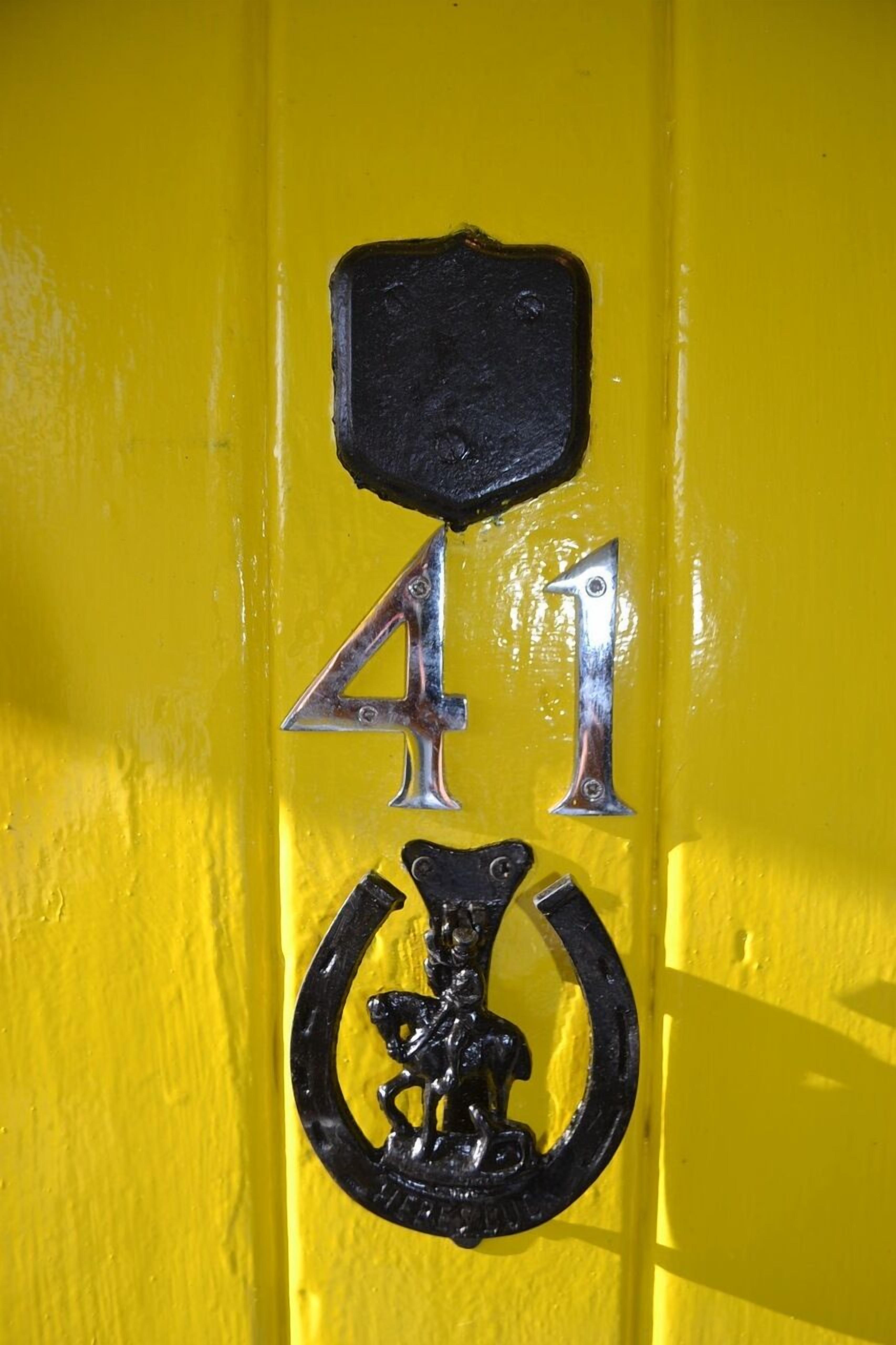 Una porta groga amb un número “41” de metall negre i un símbol de cavall de metall.