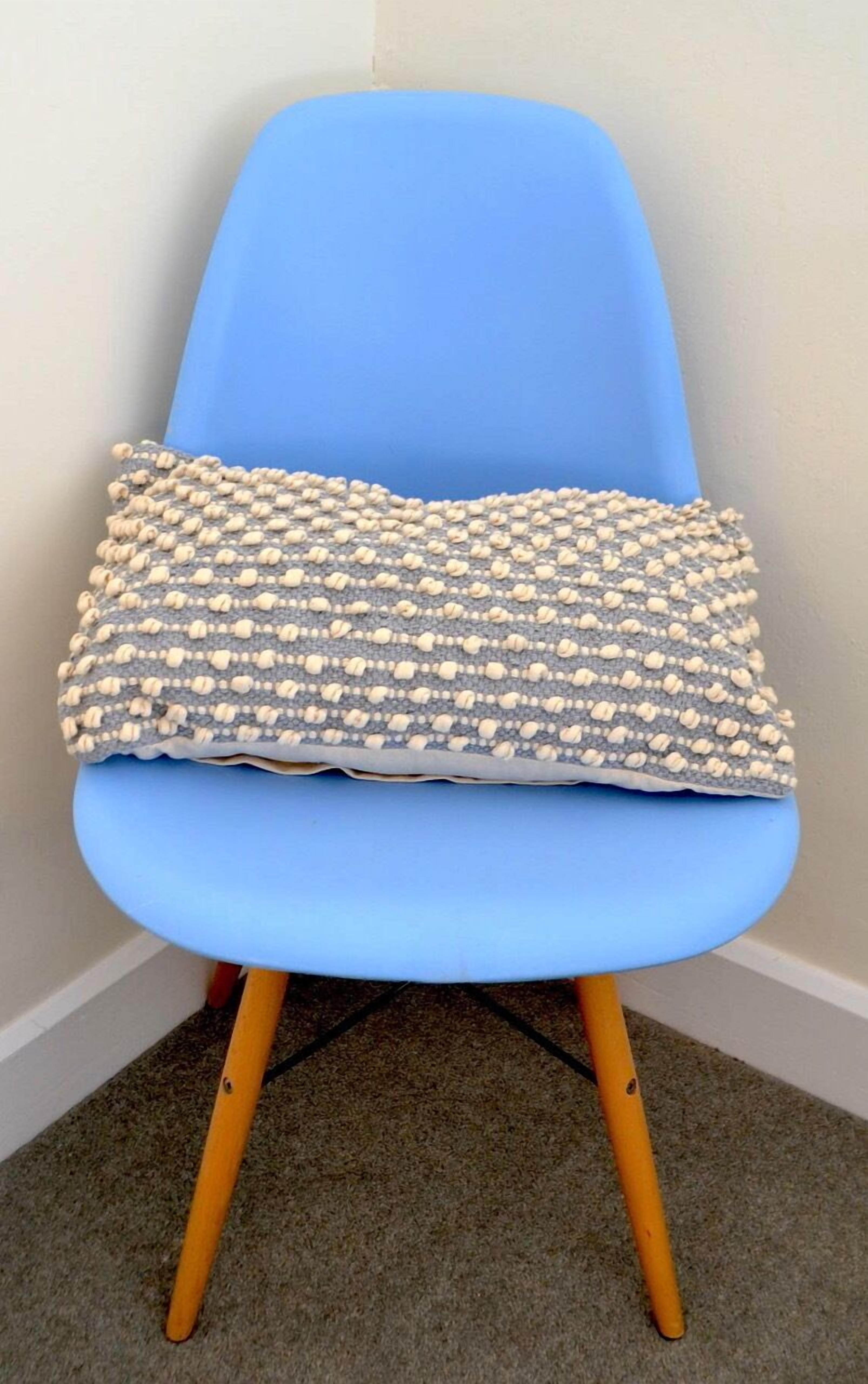 Una sedia blu con gambe di legno e un cuscino decorato.
