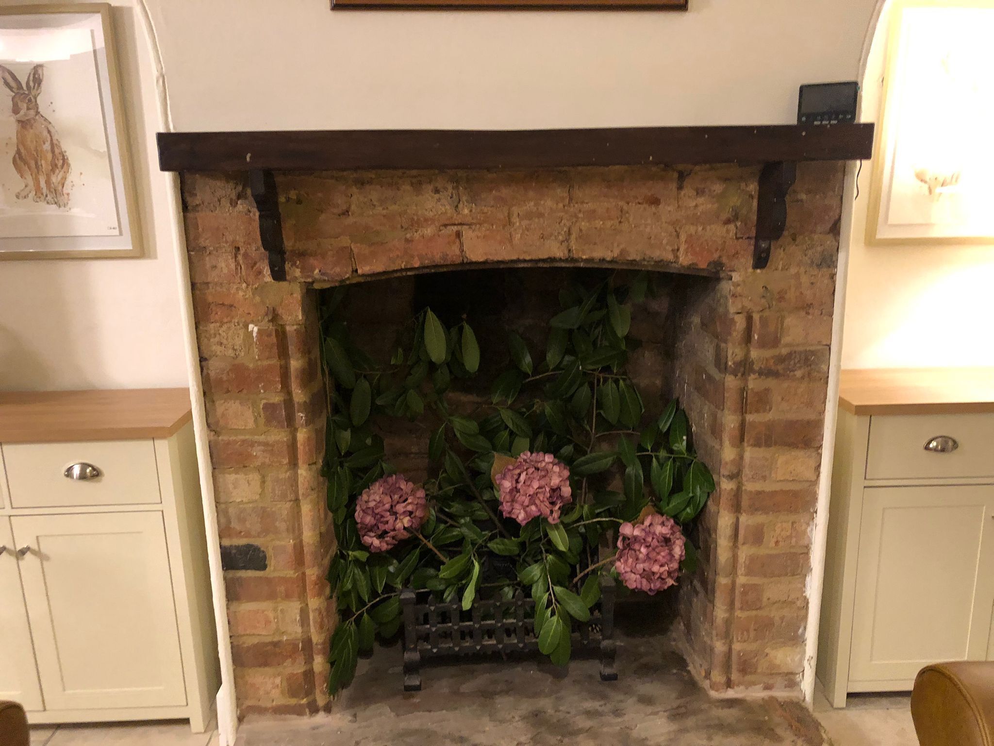 A fireplace with a brick surround, a wooden mantel, and pink hydrangea flowers.