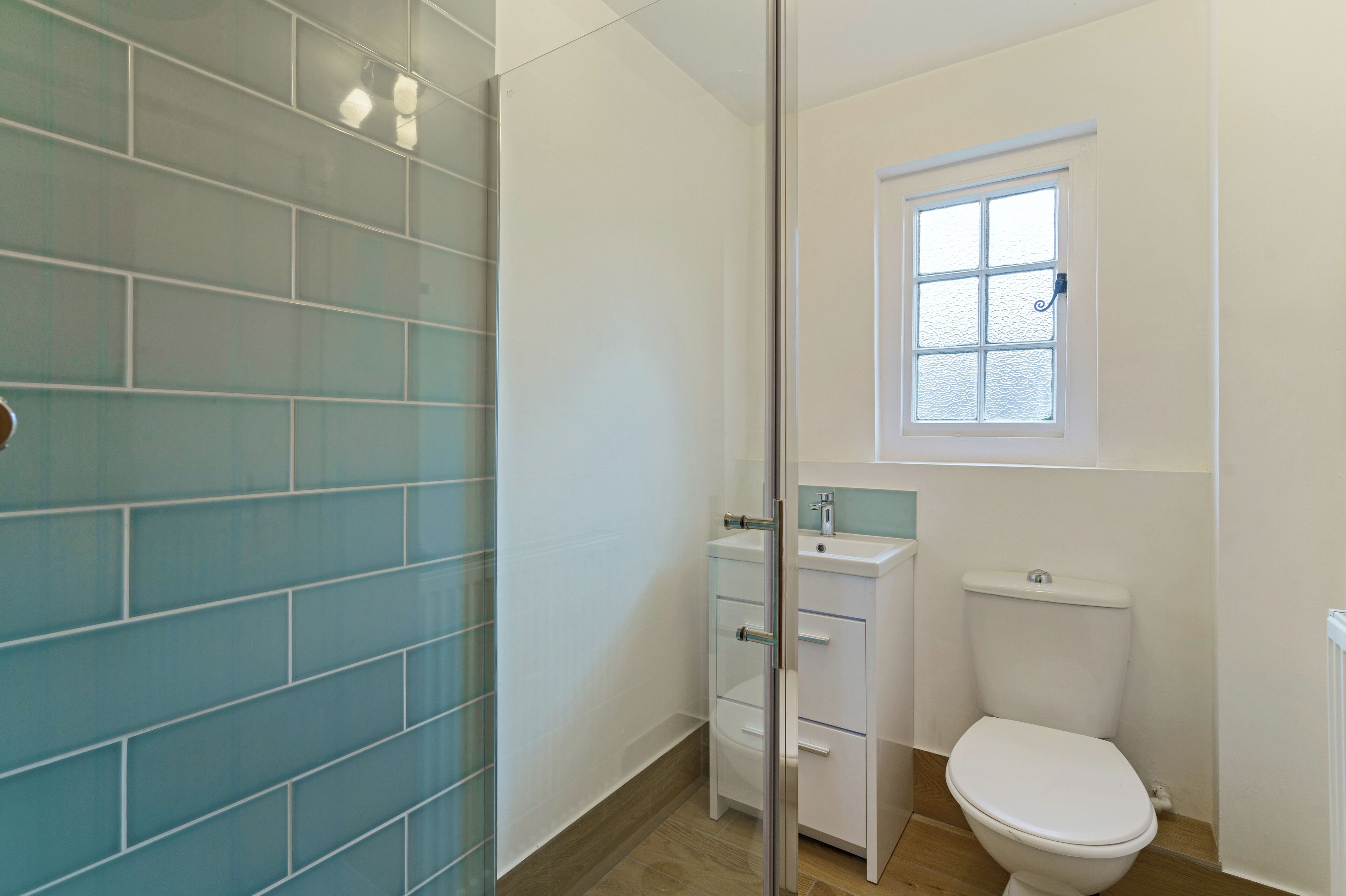 A bathroom with a glass shower enclosure, a white toilet, and a window above the toilet.
