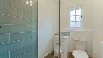 A bathroom with a glass shower enclosure, a white toilet, and a window above the toilet.