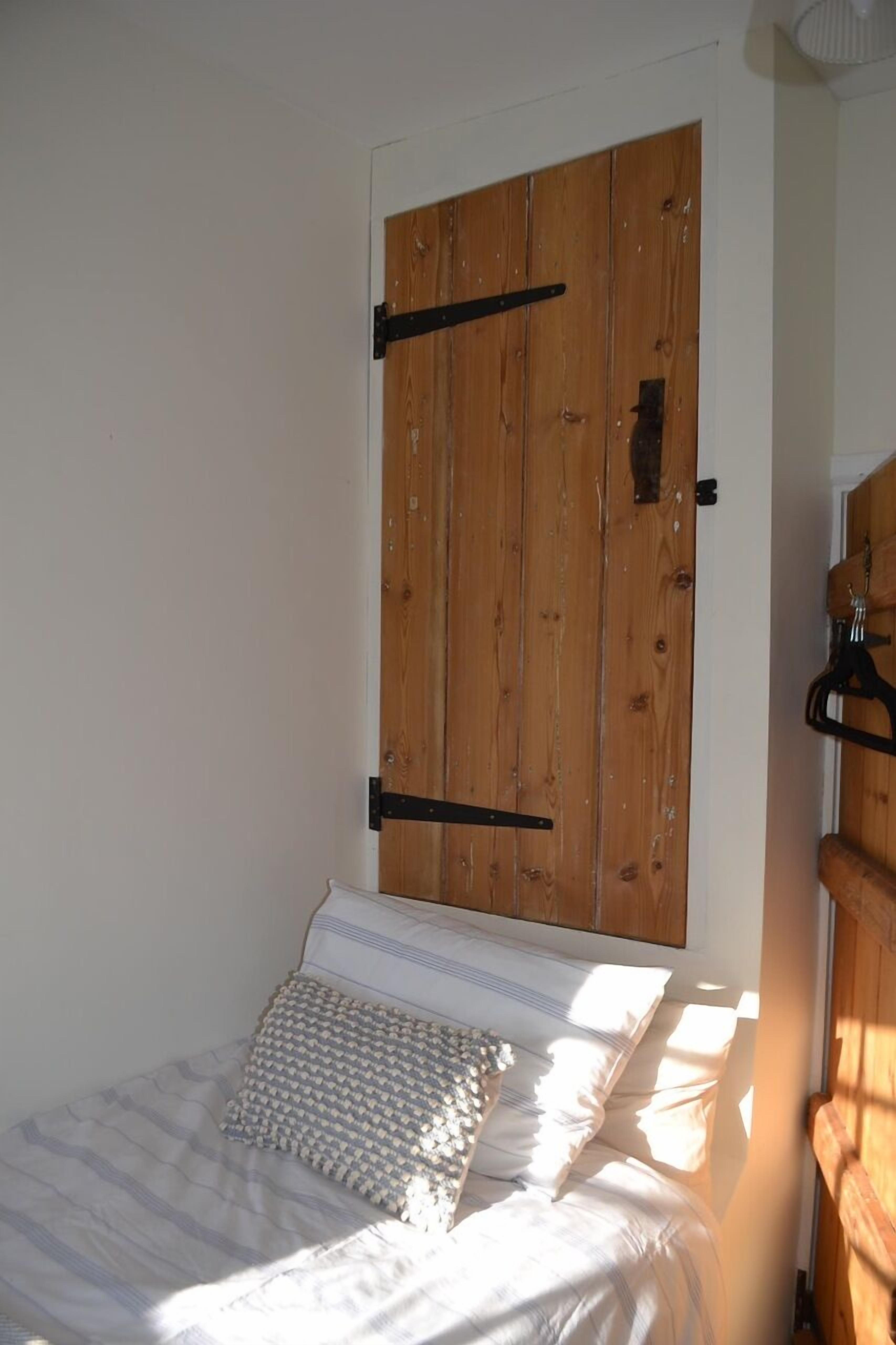 A bedroom with a bed, a wooden door, and a small wooden shelf.
