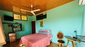 Une chambre à coucher comprenant un lit, un bureau, une chaise, un ventilateur de plafond, une télévision et un réfrigérateur.