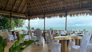 Un espace extérieur aménagé pour les repas, avec des chaises en plastique blanc et des tables en bois, donnant sur une étendue d’eau.