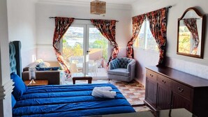 A bedroom with a bed, a chair, a small table, a wardrobe, and a balcony with curtains. - TIKI HOUSE  (Lalla Takarkoust)