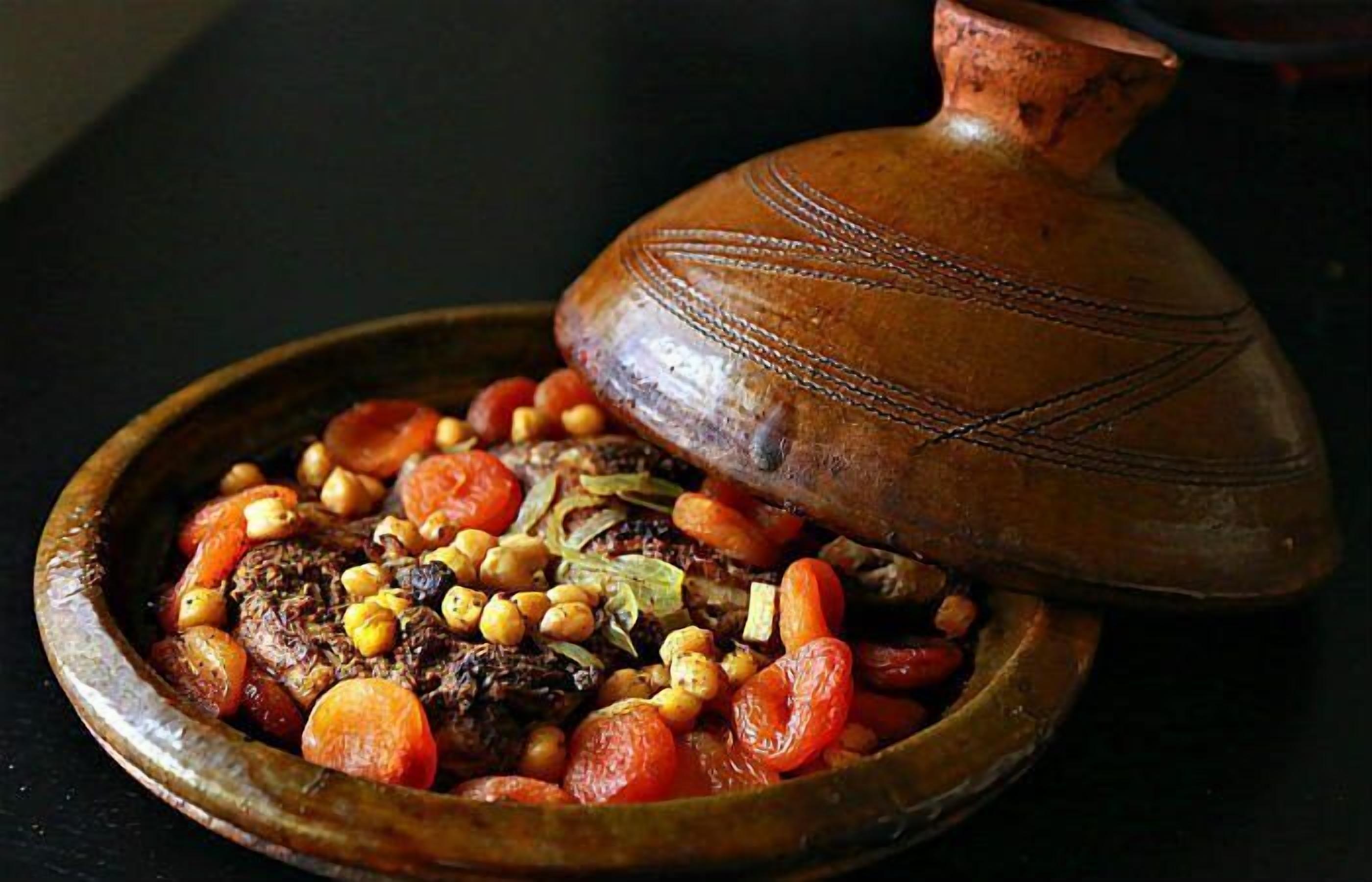 Un plat traditionnel marocain, un tajine, servi dans un plat en bois et recouvert d’un couvercle en terre cuite.