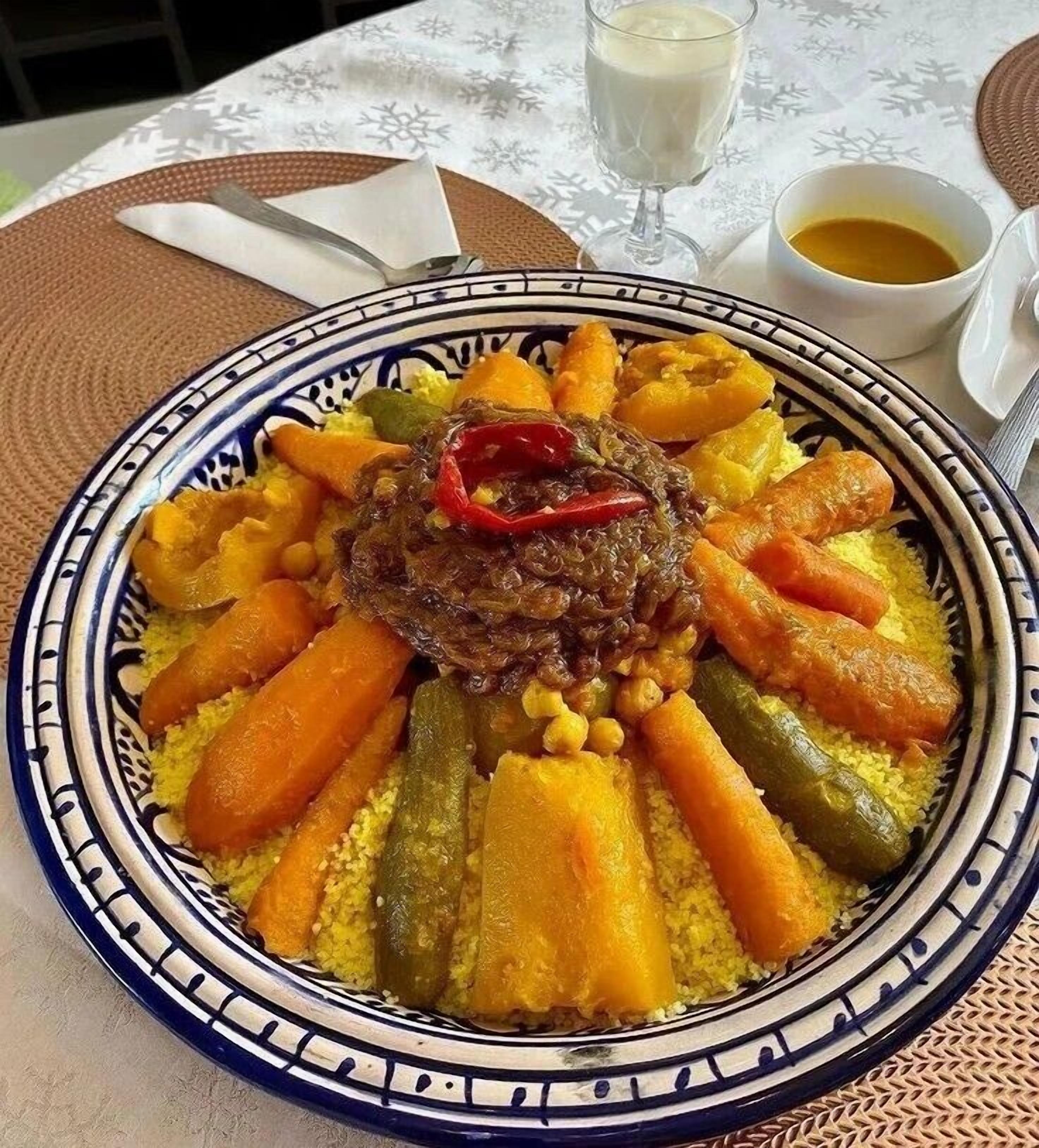 Un plato de cuscús con verduras y un guiso de carne, servido en un plato estampado.