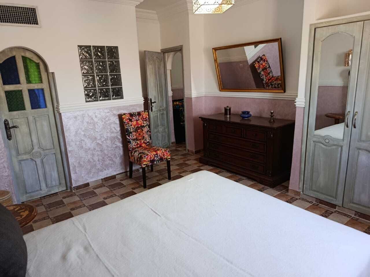 Une chambre à coucher avec un grand lit, une commode, une chaise et un miroir au mur.