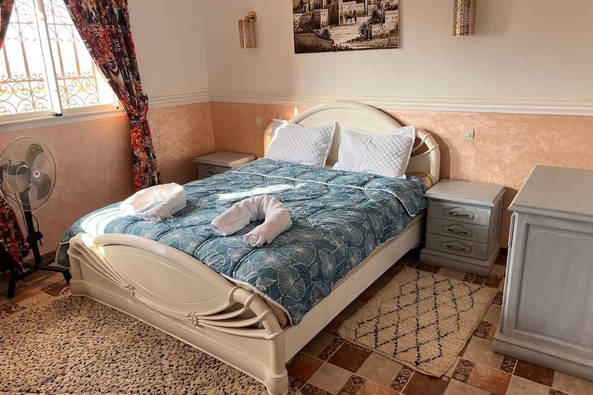 A neatly arranged bedroom with a bed, bedside tables, a fan, and a dresser.