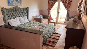A bedroom with a tufted headboard bed, a small sofa, a desk, and a patterned rug. - TIKI HOUSE  (Lalla Takarkoust)