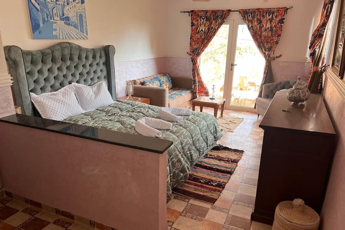 A bedroom with a tufted headboard bed, a small sofa, a desk, and a patterned rug.