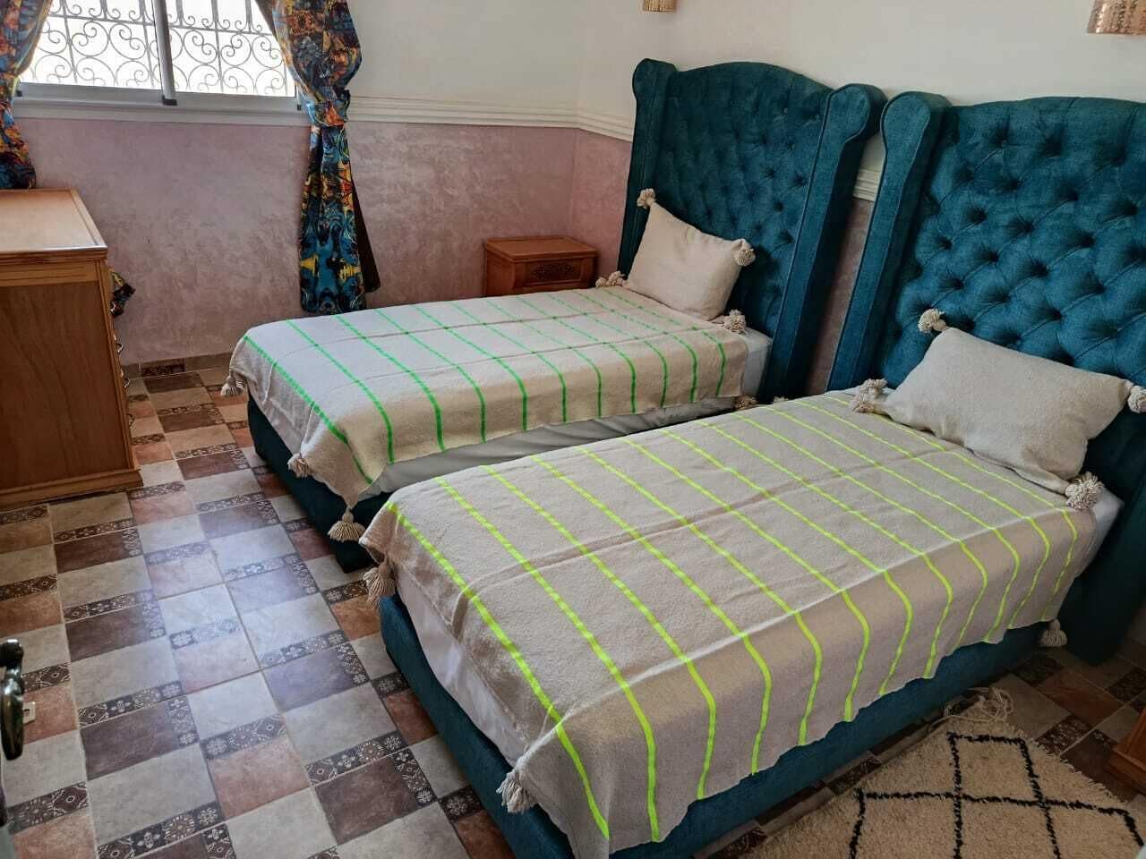 Ein Schlafzimmer mit zwei Betten, einem hölzernen Schminktisch und einem Fenster mit Vorhängen.