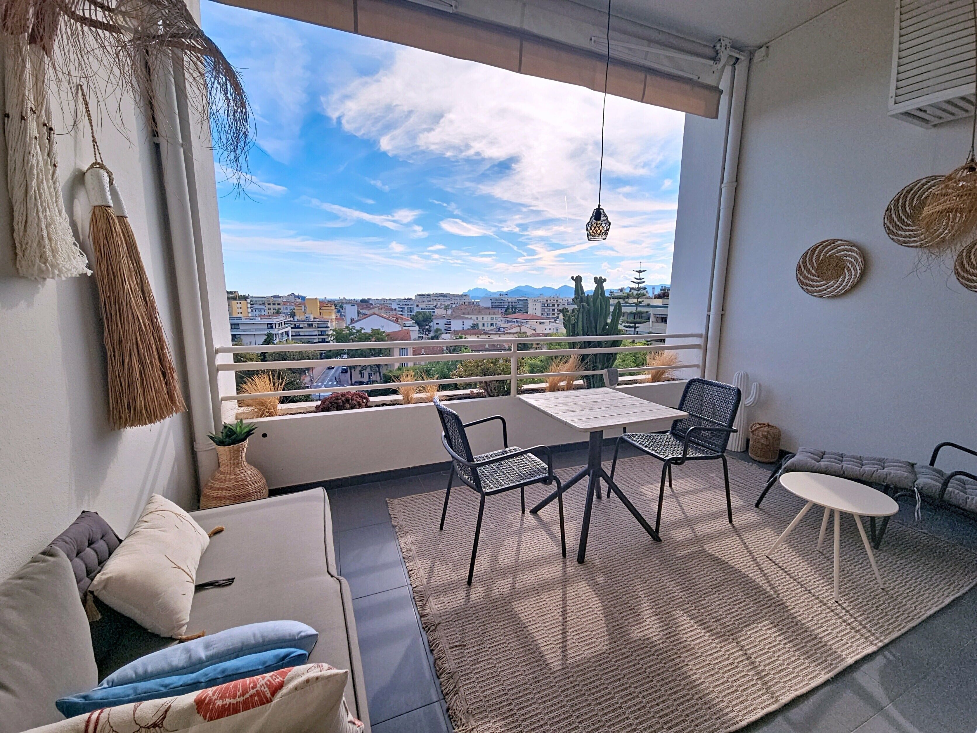 A balcony with a view of a cityscape, a table with chairs, and a sofa with cushions.