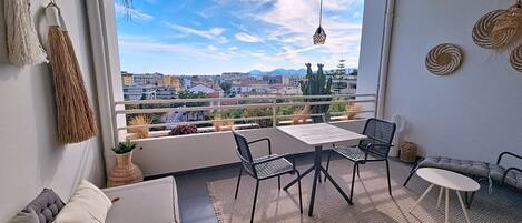 A balcony with a view of a cityscape, a table with chairs, and a sofa with cushions.