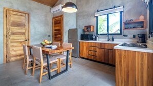 A modern kitchen with wooden cabinets, a dining table with chairs, and a fruit bowl. - Bali-Style Jungle Bungalow, salt water pool, near beaches. (Ojochal)