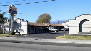 A motel with a signboard, a parking lot, and a mountainous background.