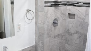 A modern bathroom with a white sink, a glass shower enclosure, and marble walls.