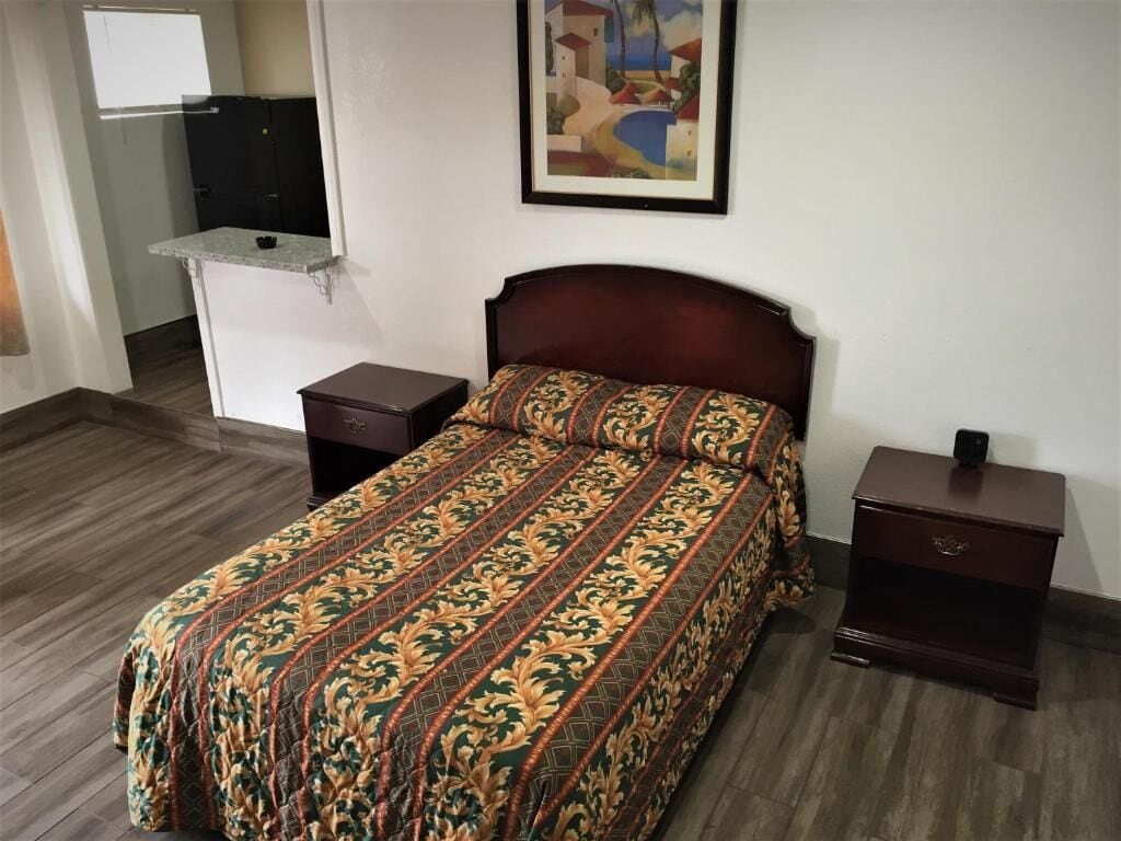 A bedroom with a bed, nightstands, a dresser, and a painting on the wall.