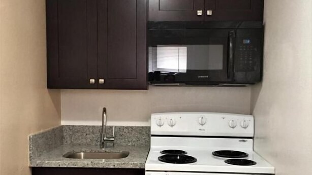 A compact kitchen with dark cabinets, a microwave, and a white stove.