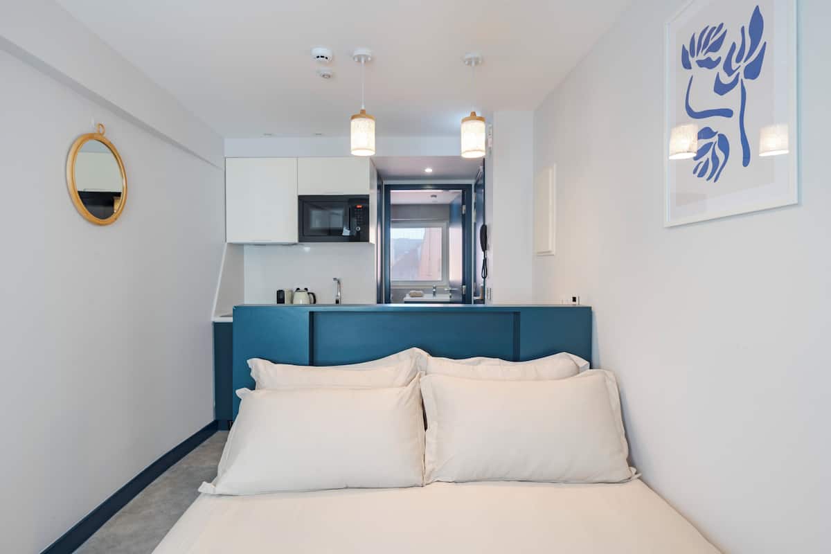 Ein Hotelzimmer mit Bett, einer Küchenzeile, einem Badezimmer und einem Flur, der in ein weiteres Zimmer führt.