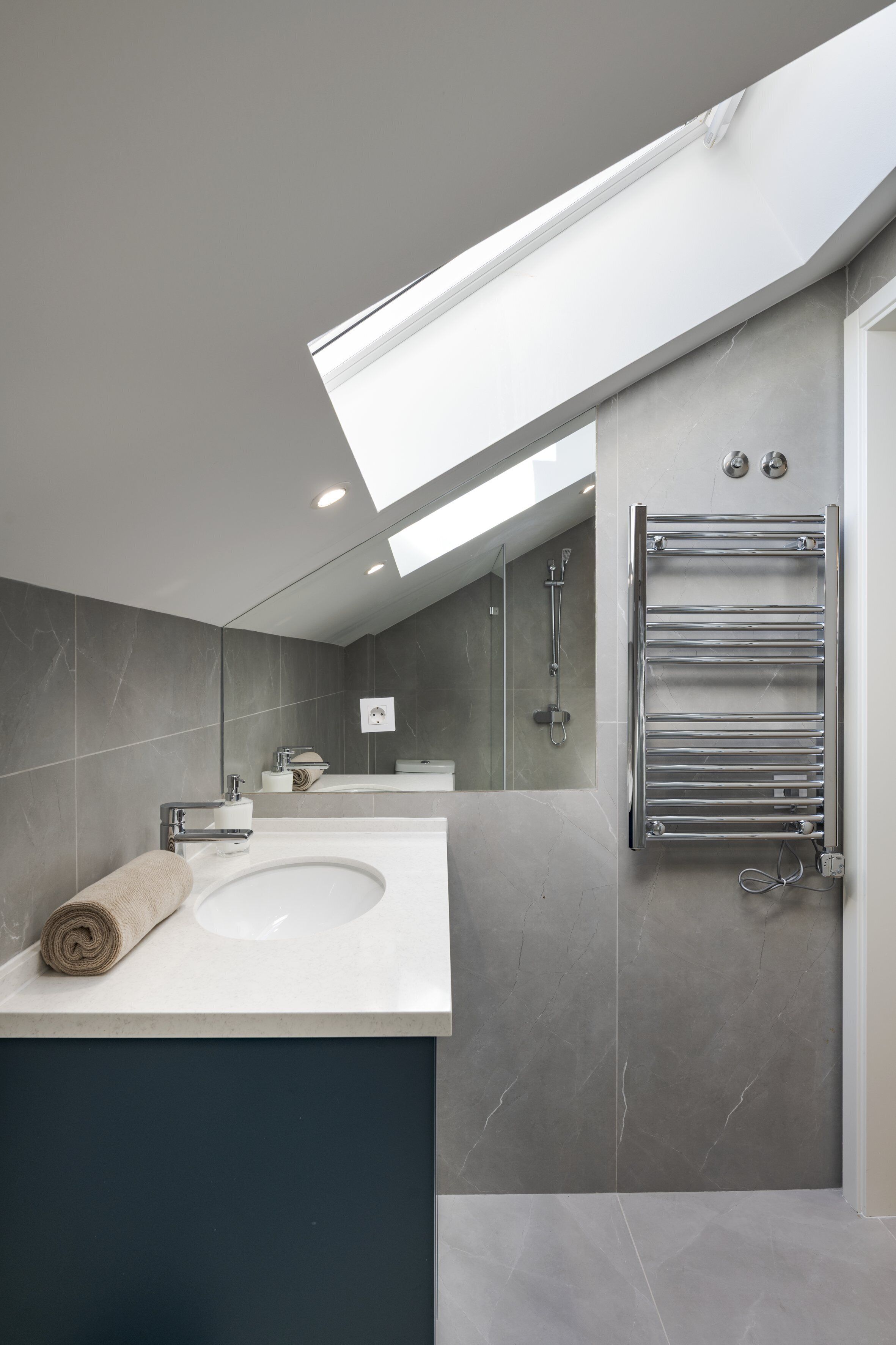 A modern bathroom with a skylight, a large sink, and a towel rack.