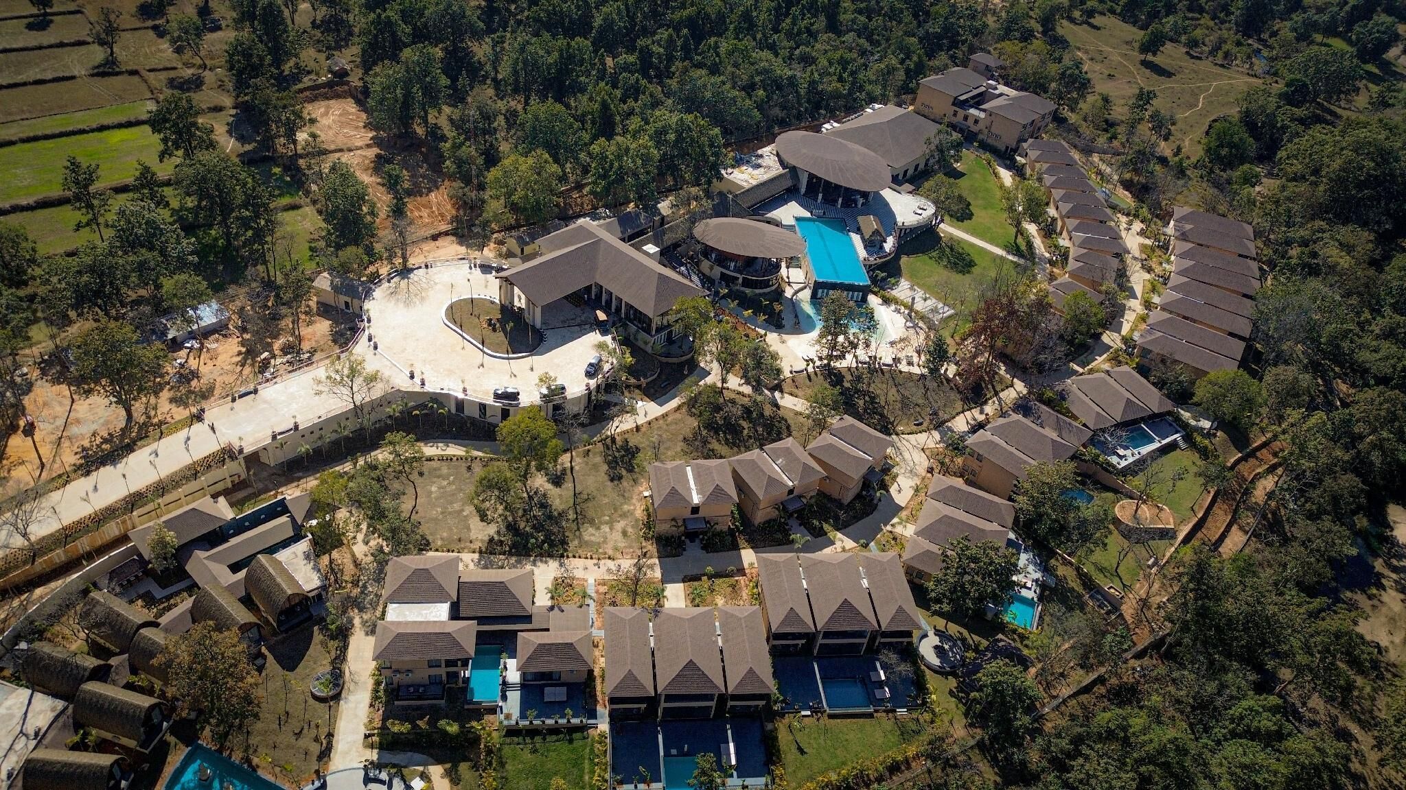 Vista aérea de un resort con varias cabañas, un edificio central con piscina y zonas ajardinadas alrededor.