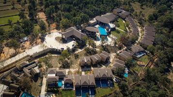 Vista aérea de un resort con varias cabañas, un edificio central con piscina y zonas ajardinadas alrededor.