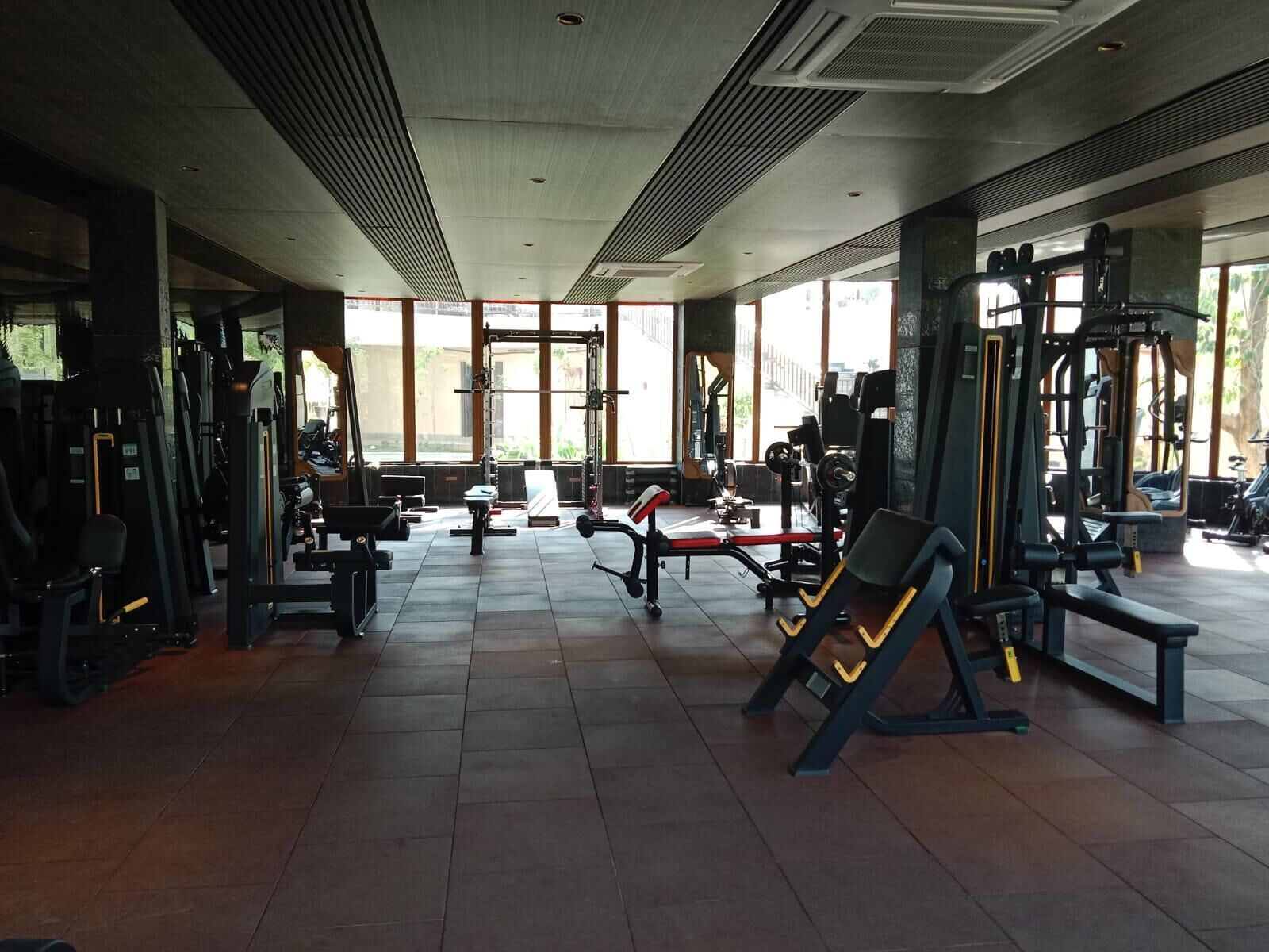 Een sportschool met diverse fitnessapparaten, grote ramen en een betegelde vloer.