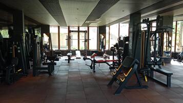 Een sportschool met diverse fitnessapparaten, grote ramen en een betegelde vloer.