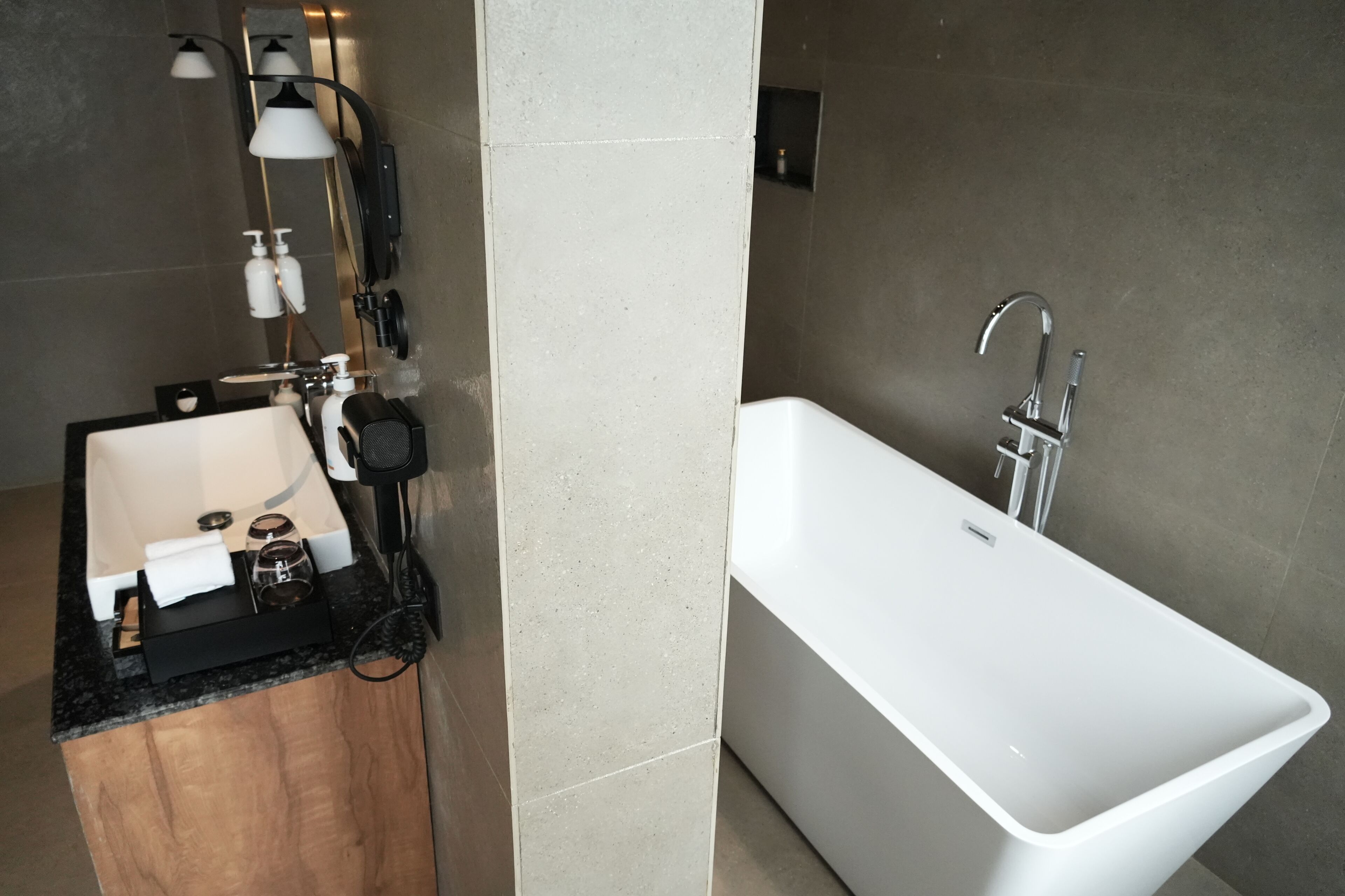 A modern bathroom with a white bathtub, a sink, and a mirror. There are two wall-mounted lights and a hairdryer on the counter.