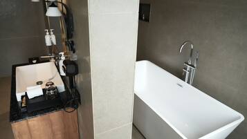A modern bathroom with a white bathtub, a sink, and a mirror. There are two wall-mounted lights and a hairdryer on the counter.