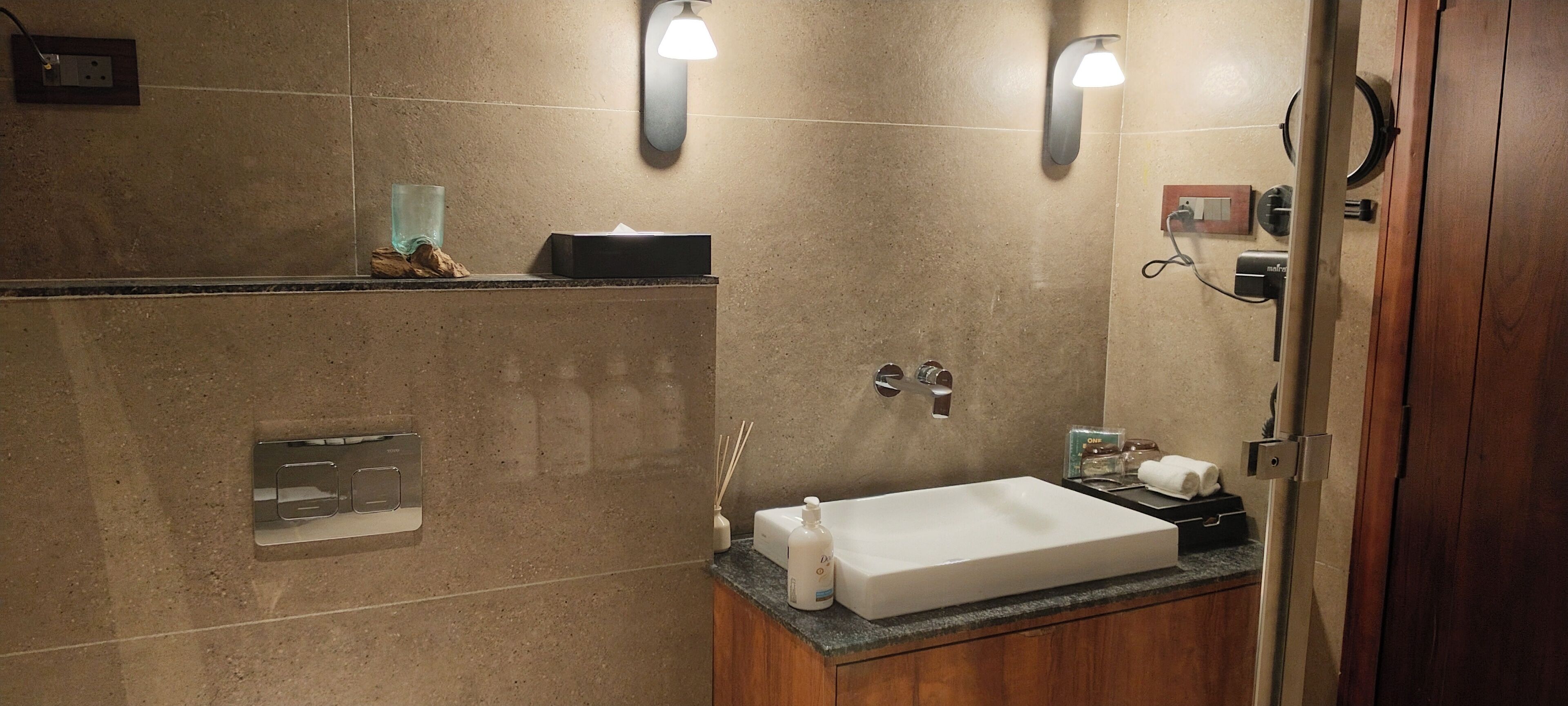 A bathroom with a large sink, two wall-mounted light fixtures, a mirror, and a towel rack.