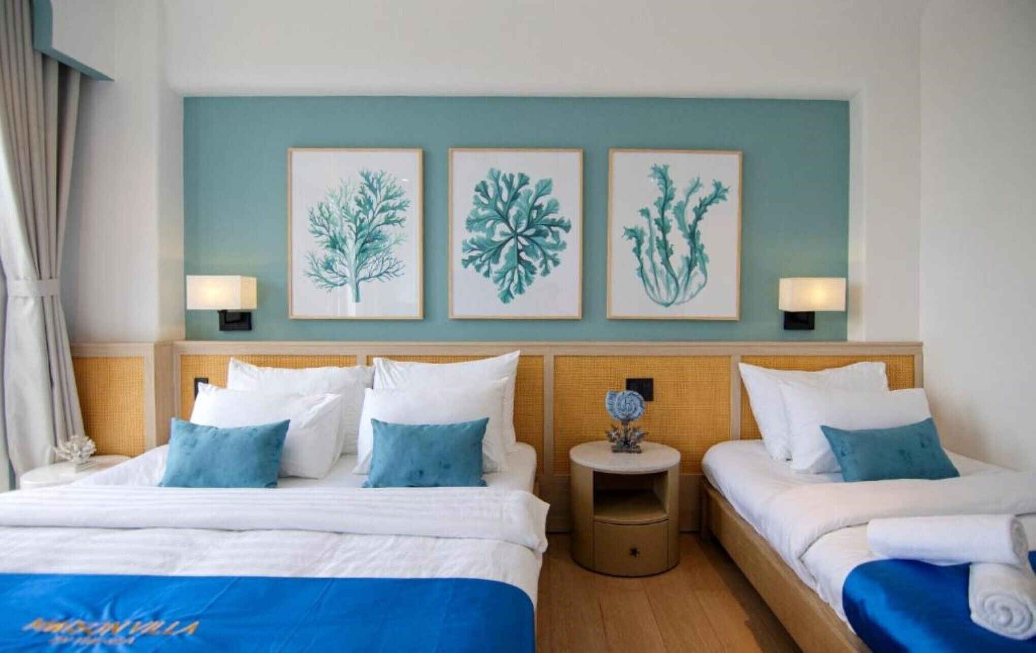 A hotel room with two beds, a blue bedspread, white bedding, and three framed wall art pieces.