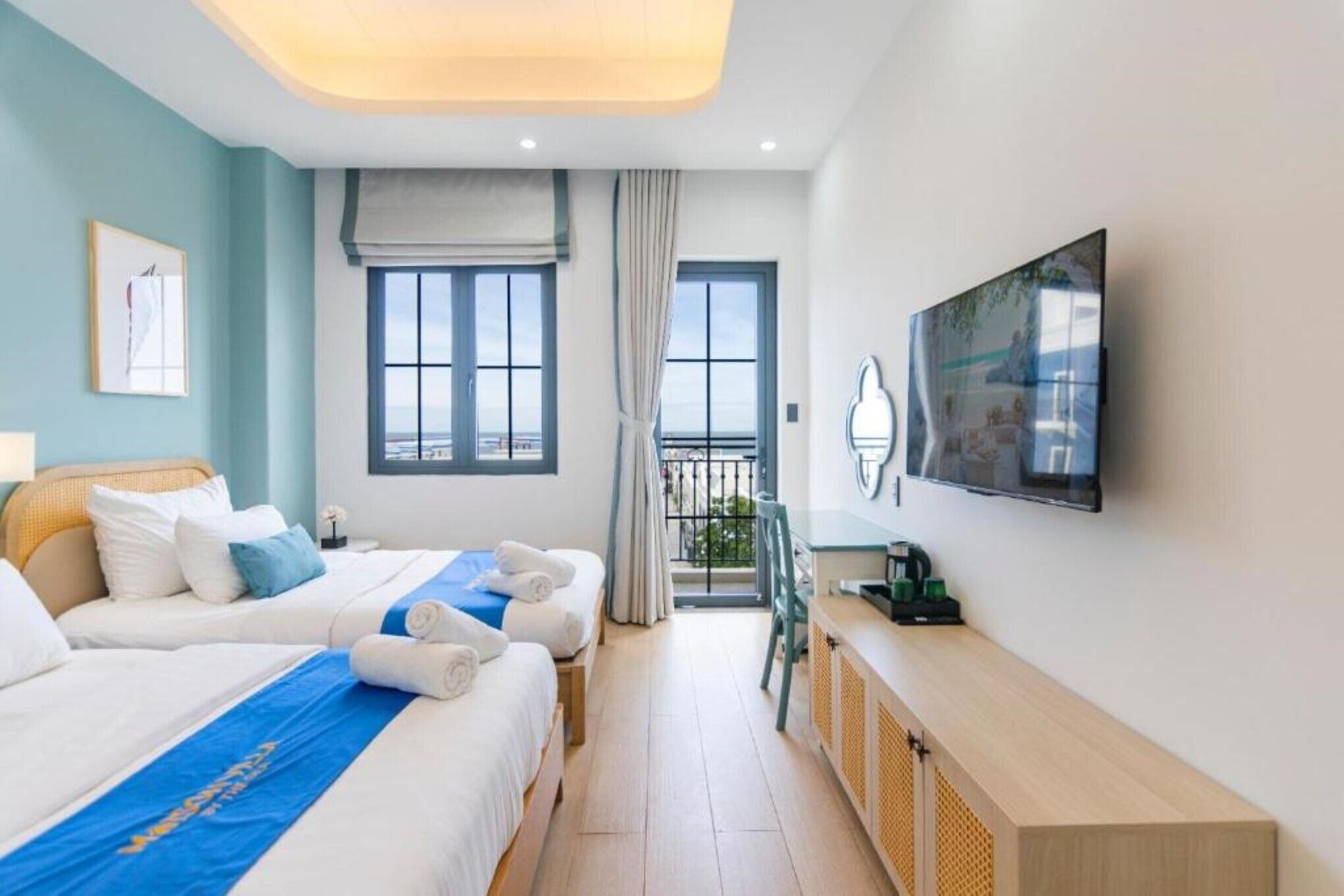 A hotel room with two beds, a TV, a balcony, and a view of the sea.