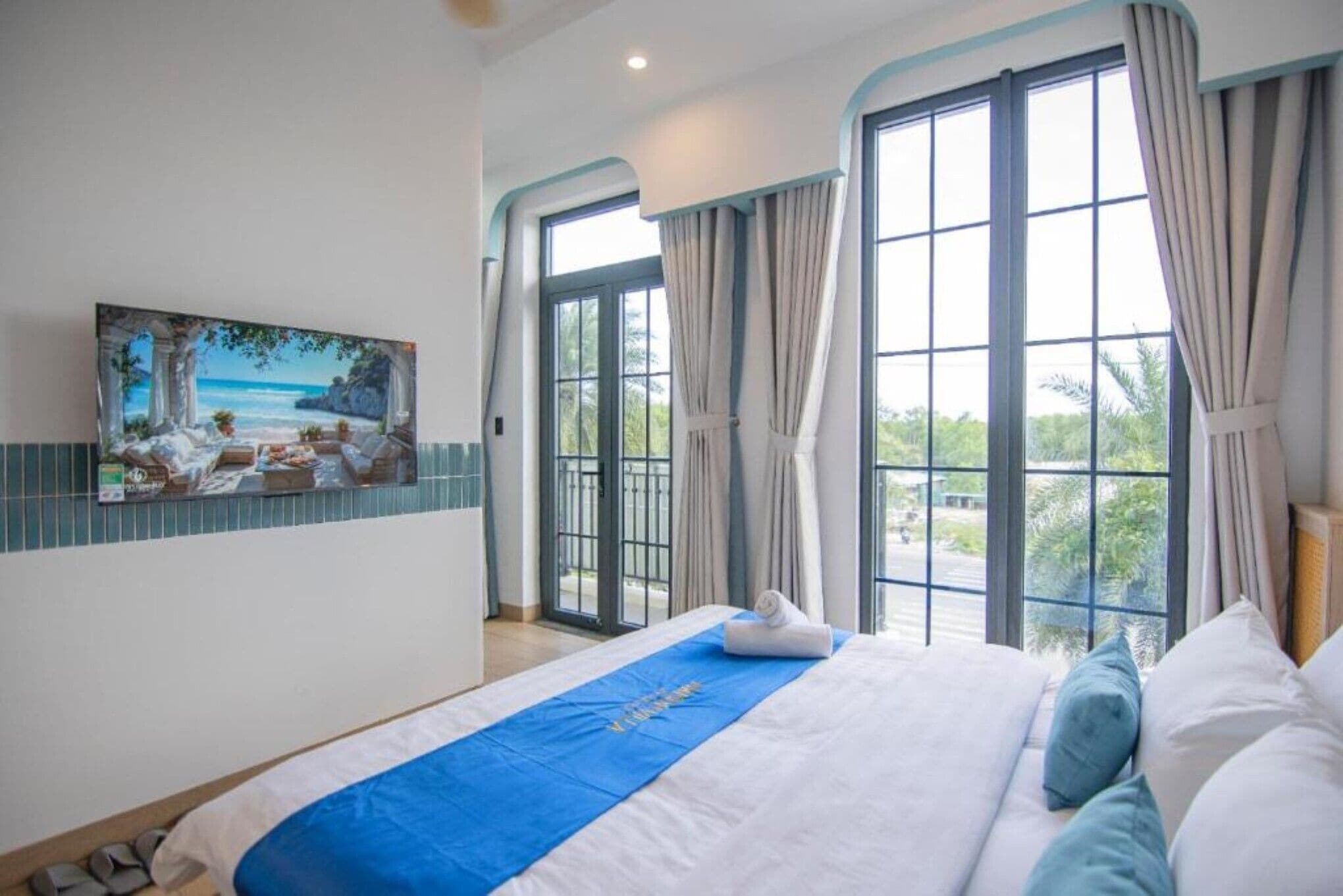 Habitación de hotel con una cama grande, un cuadro de una playa y vistas al exterior a través de amplios ventanales.